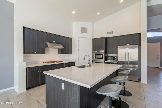 kitchen with high vaulted ceiling, sink, an island with sink, appliances with stainless steel finishes, and a kitchen bar