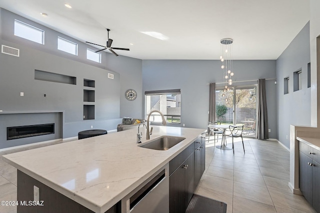 kitchen with pendant lighting, high vaulted ceiling, a center island with sink, sink, and stainless steel dishwasher