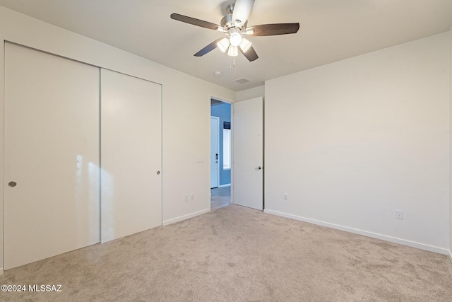 unfurnished bedroom with a closet, light colored carpet, and ceiling fan