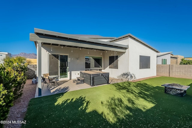 back of property with a fire pit, a patio, a lawn, and a hot tub