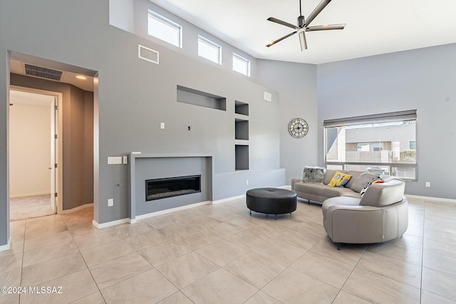 living room featuring built in shelves, ceiling fan, light tile patterned floors, and a high ceiling