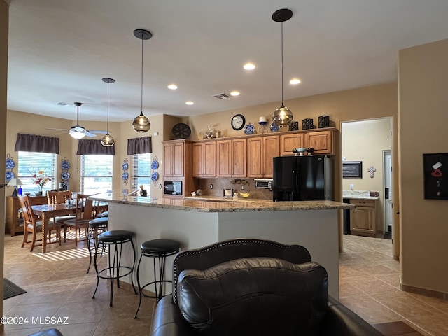 kitchen featuring light tile patterned flooring, decorative backsplash, hanging light fixtures, black fridge, and light stone countertops