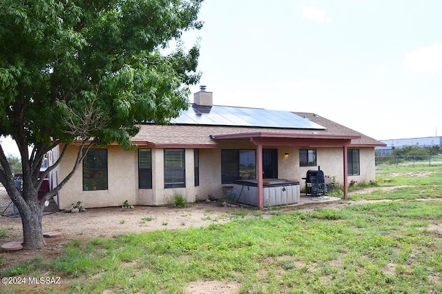 rear view of property featuring stucco siding, roof mounted solar panels, a chimney, and a hot tub