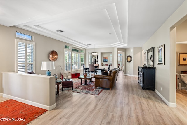 living room with light wood-type flooring, a raised ceiling, and a wealth of natural light