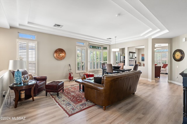 living room featuring ceiling fan, light wood-type flooring, a raised ceiling, and a wealth of natural light