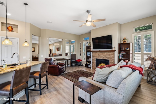 living room with light wood-type flooring, ceiling fan, and a stone fireplace