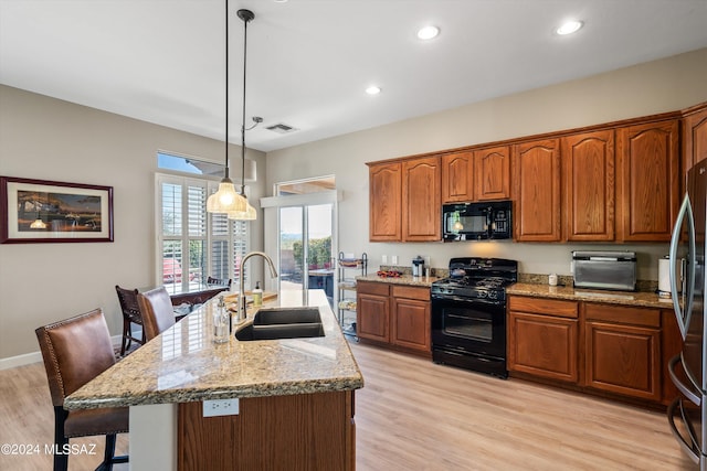 kitchen with a kitchen island with sink, sink, a kitchen breakfast bar, black appliances, and decorative light fixtures