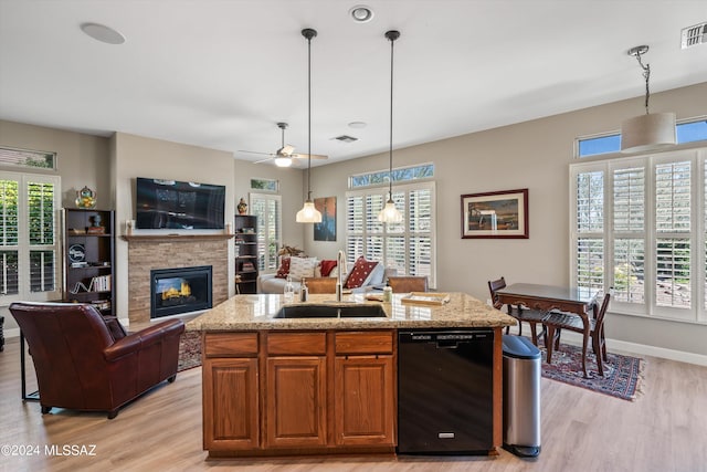 kitchen with an island with sink, sink, a fireplace, black dishwasher, and light wood-type flooring