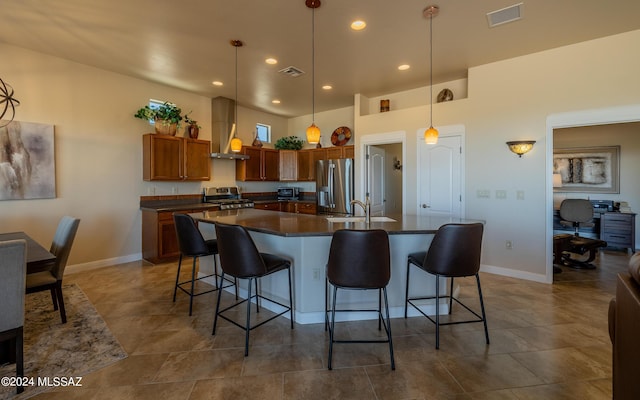 kitchen with stainless steel appliances, a kitchen island with sink, sink, wall chimney range hood, and decorative light fixtures