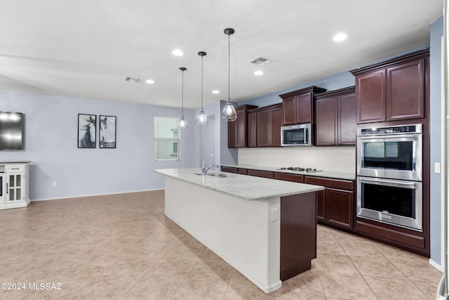 kitchen featuring light stone counters, sink, decorative light fixtures, a kitchen island with sink, and appliances with stainless steel finishes