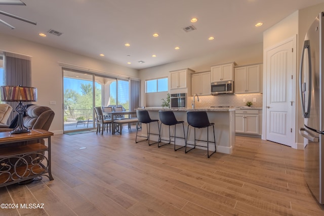 kitchen with a center island with sink, white cabinets, light stone countertops, light hardwood / wood-style floors, and stainless steel appliances