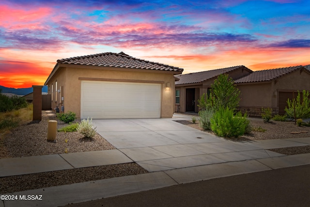 view of front facade featuring a garage, driveway, a tile roof, and stucco siding