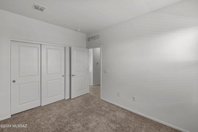 unfurnished bedroom with light colored carpet and a closet