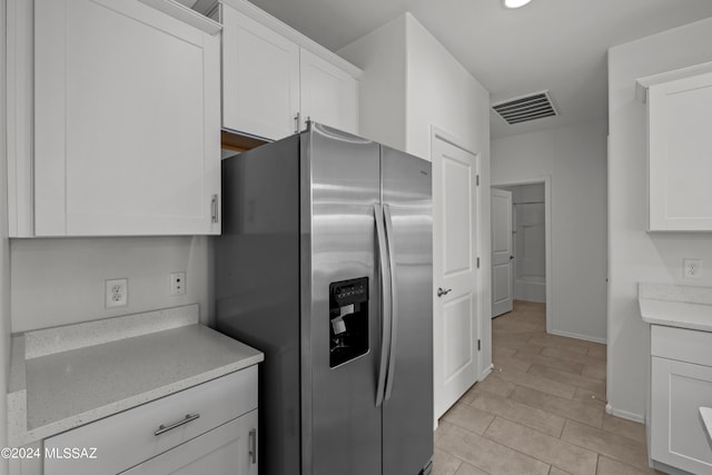 kitchen with light stone counters, visible vents, baseboards, white cabinetry, and stainless steel refrigerator with ice dispenser