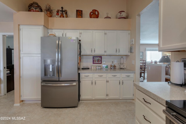 kitchen featuring stainless steel fridge, light tile patterned floors, and white cabinetry