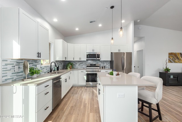 kitchen featuring white cabinetry, sink, lofted ceiling, a kitchen island, and appliances with stainless steel finishes