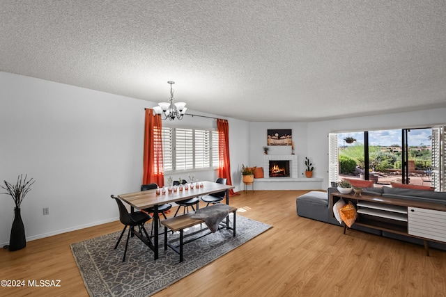 dining room with an inviting chandelier, a brick fireplace, wood-type flooring, and a textured ceiling