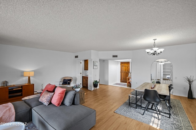 living room with a notable chandelier, light wood-type flooring, and a textured ceiling