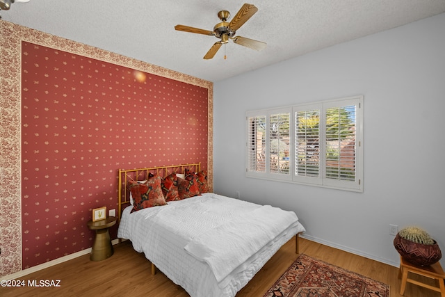 bedroom with hardwood / wood-style floors, ceiling fan, and a textured ceiling