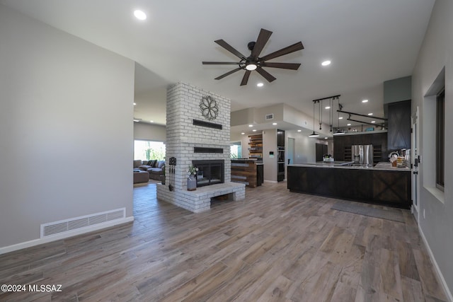 living room featuring light wood-style flooring, a brick fireplace, visible vents, and recessed lighting