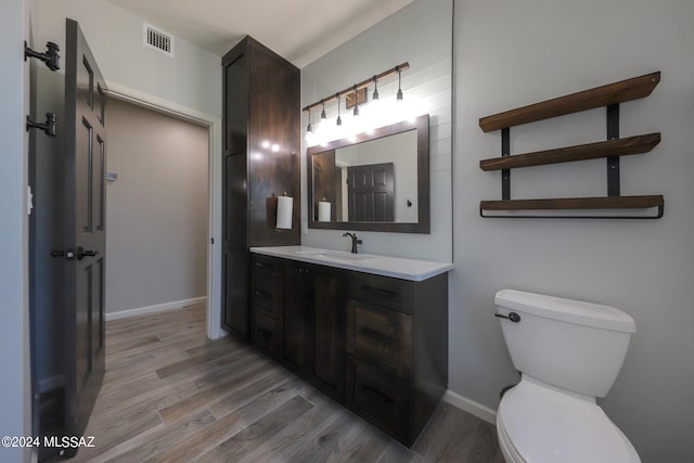 half bathroom featuring visible vents, vanity, toilet, and wood finished floors