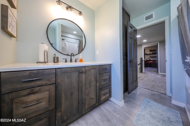 bathroom with a walk in closet, visible vents, vanity, and baseboards