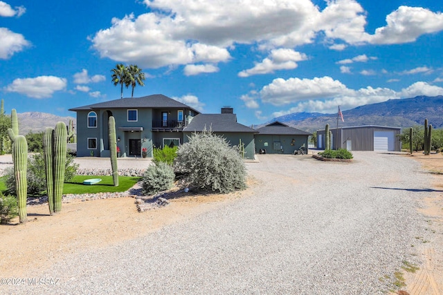 view of front of home with gravel driveway, a mountain view, a balcony, a garage, and an outdoor structure