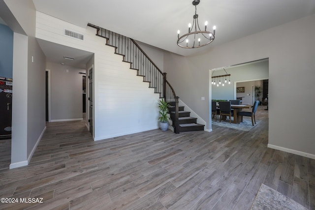 entrance foyer with visible vents, wood finished floors, a chandelier, baseboards, and stairs