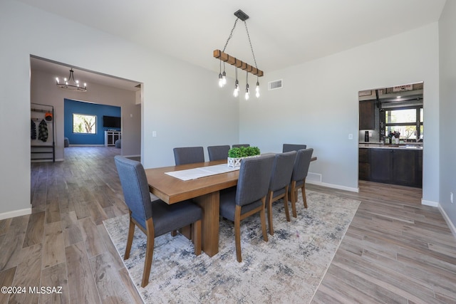 dining room featuring light wood finished floors, lofted ceiling, visible vents, a chandelier, and baseboards