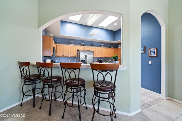 kitchen featuring baseboards, arched walkways, light tile patterned floors, and stainless steel refrigerator with ice dispenser