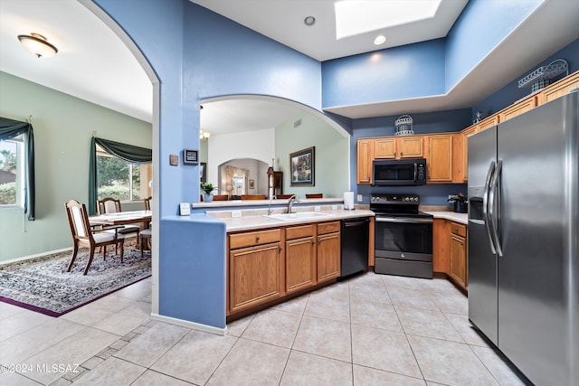 kitchen with light countertops, stainless steel appliances, a sink, brown cabinetry, and light tile patterned floors