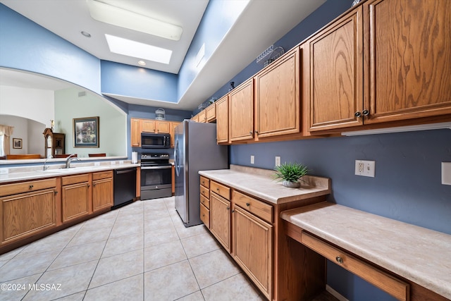kitchen with light tile patterned flooring, a sink, a skylight, brown cabinets, and black appliances
