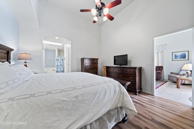 bedroom with arched walkways, high vaulted ceiling, wood finished floors, and ensuite bathroom