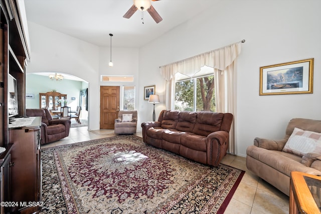 living room with arched walkways, light tile patterned floors, a high ceiling, and ceiling fan with notable chandelier
