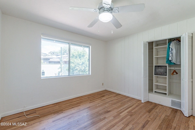 empty room with ceiling fan, wooden walls, and light wood-type flooring