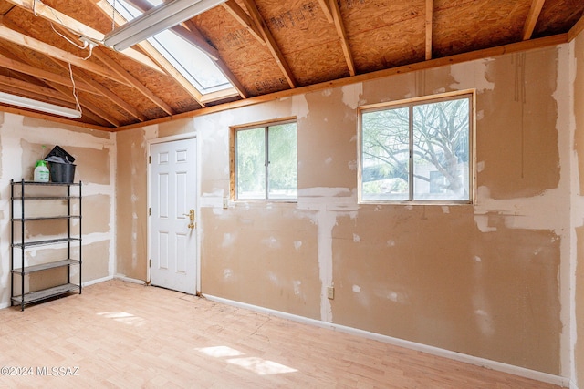 unfurnished room featuring vaulted ceiling with skylight and light wood-type flooring