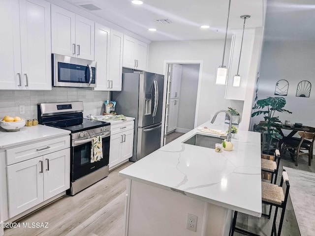 kitchen with appliances with stainless steel finishes, a breakfast bar, white cabinets, decorative light fixtures, and sink