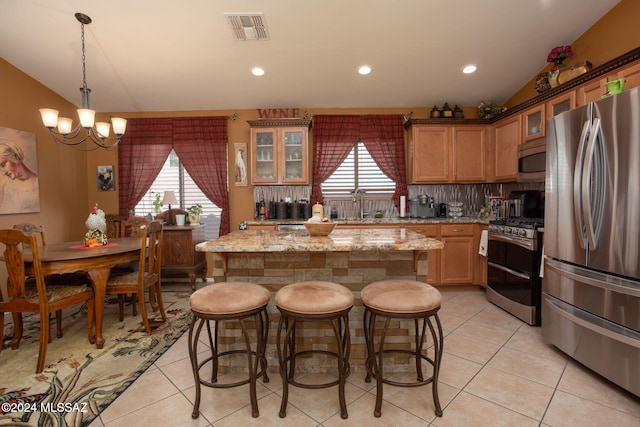 kitchen with light tile patterned floors, appliances with stainless steel finishes, light stone countertops, decorative light fixtures, and a center island