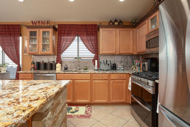 kitchen with stainless steel appliances, sink, light stone countertops, light tile patterned floors, and tasteful backsplash