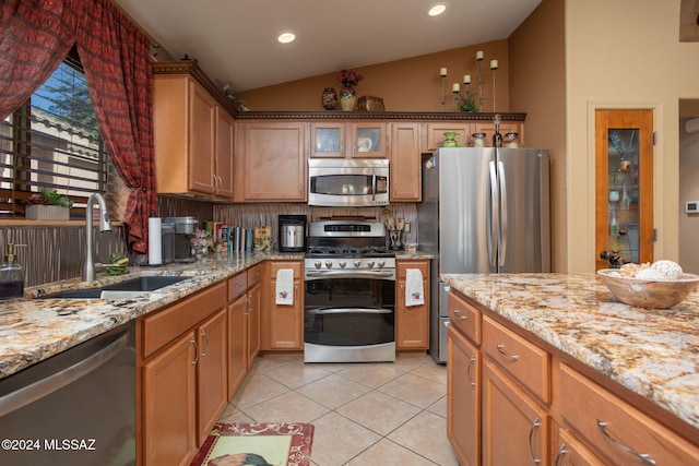 kitchen featuring light tile patterned floors, appliances with stainless steel finishes, light stone countertops, vaulted ceiling, and sink