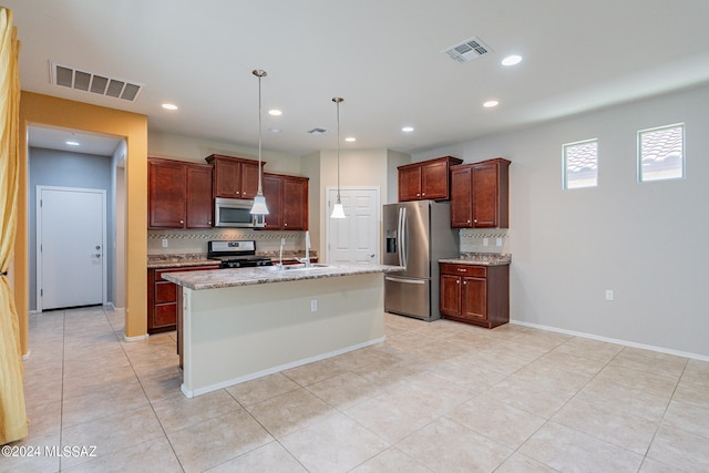 kitchen featuring a kitchen island with sink, light tile patterned floors, light stone countertops, decorative light fixtures, and stainless steel appliances