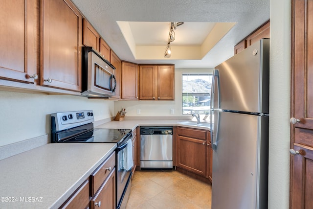 kitchen with a sink, light countertops, appliances with stainless steel finishes, brown cabinetry, and a raised ceiling