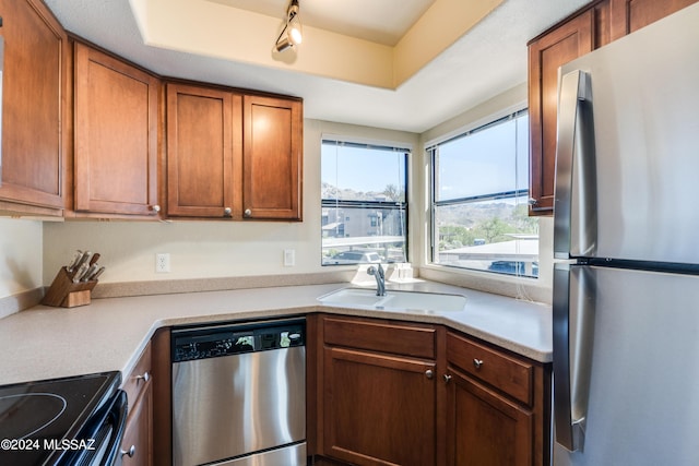 kitchen with brown cabinetry, stainless steel appliances, a sink, and light countertops