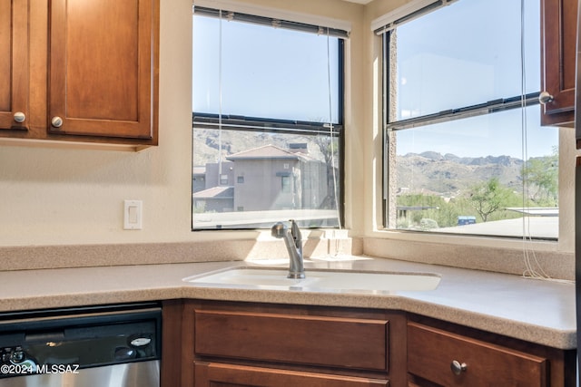 kitchen with brown cabinetry, light countertops, stainless steel dishwasher, a mountain view, and a sink