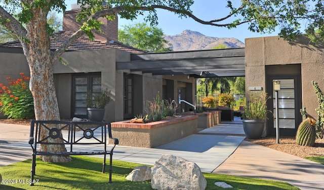 view of front of house featuring a mountain view, a tile roof, stucco siding, a chimney, and a patio area