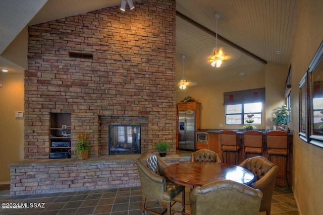 dining space featuring a stone fireplace and high vaulted ceiling