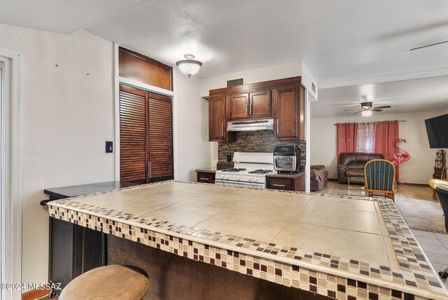 kitchen with decorative backsplash, tile patterned flooring, ceiling fan, and white gas range oven