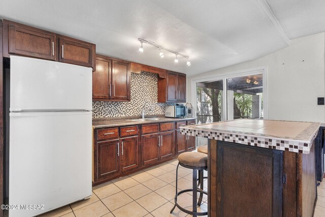 kitchen featuring a kitchen breakfast bar, light tile patterned flooring, vaulted ceiling, white refrigerator, and a center island