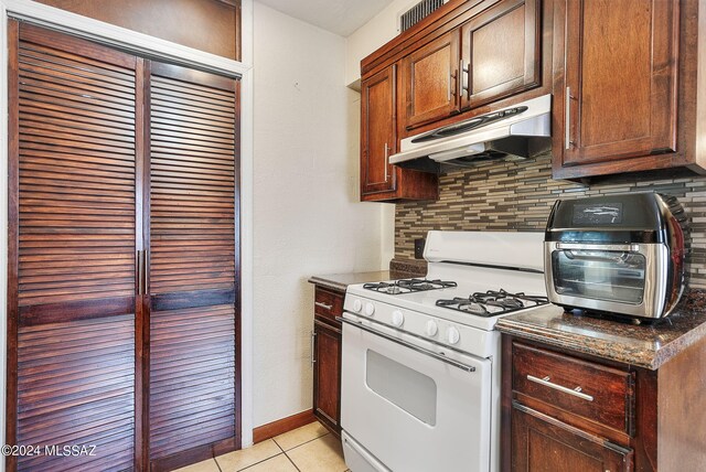 kitchen with dark stone countertops, light tile patterned floors, tasteful backsplash, and white range with gas cooktop