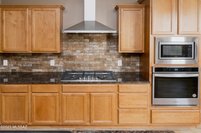 kitchen with dark stone countertops, backsplash, stainless steel appliances, and wall chimney range hood